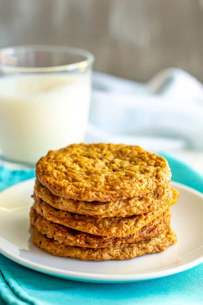 A stack of peanut butter oatmeal cookies on a white plate with a glass of milk in the background