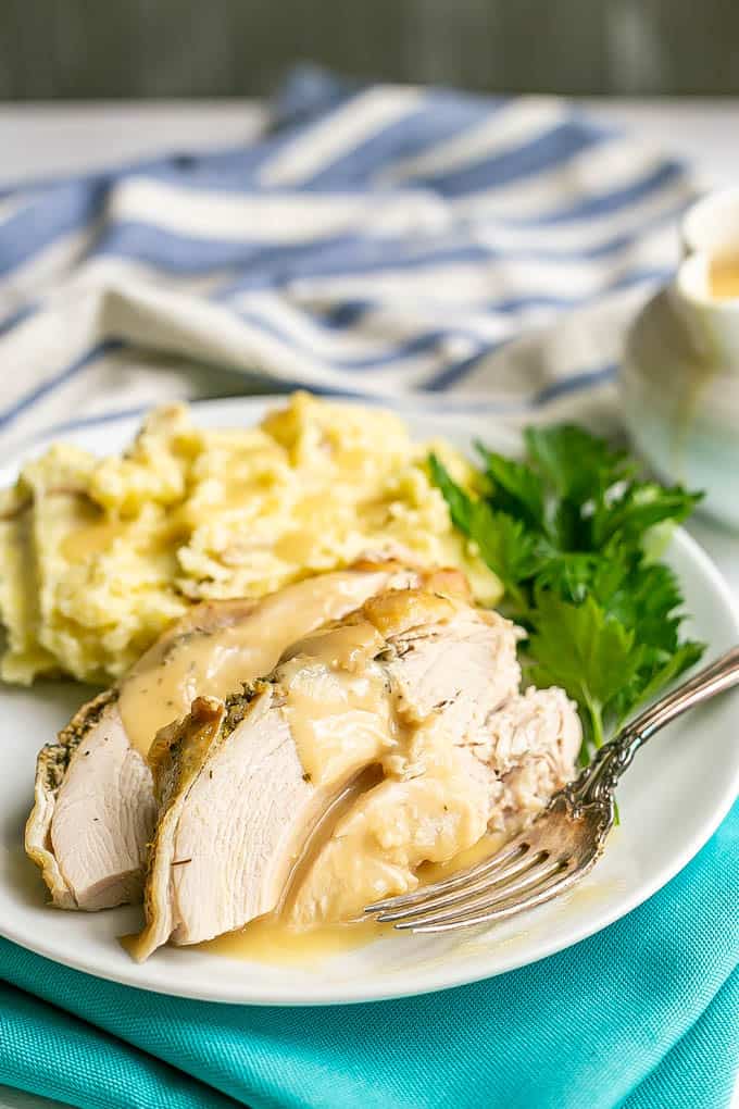 Sliced cooked turkey breast with gravy on a plate with mashed potatoes and parsley and a fork