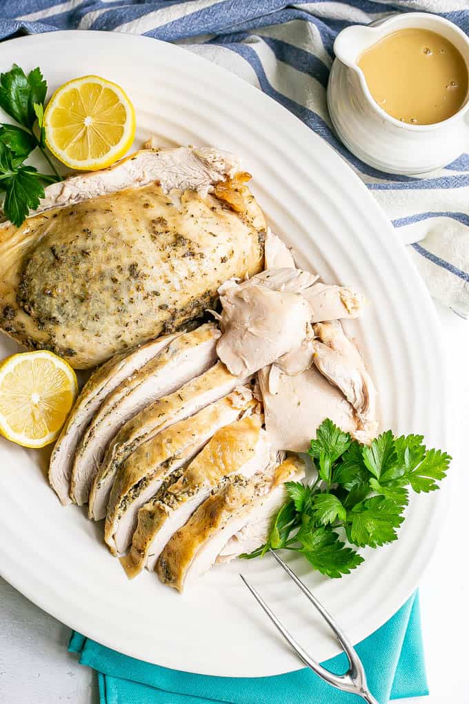 A serving platter of herb roasted slow cooker turkey breast sliced and plated with lemon halves and parsley for garnish