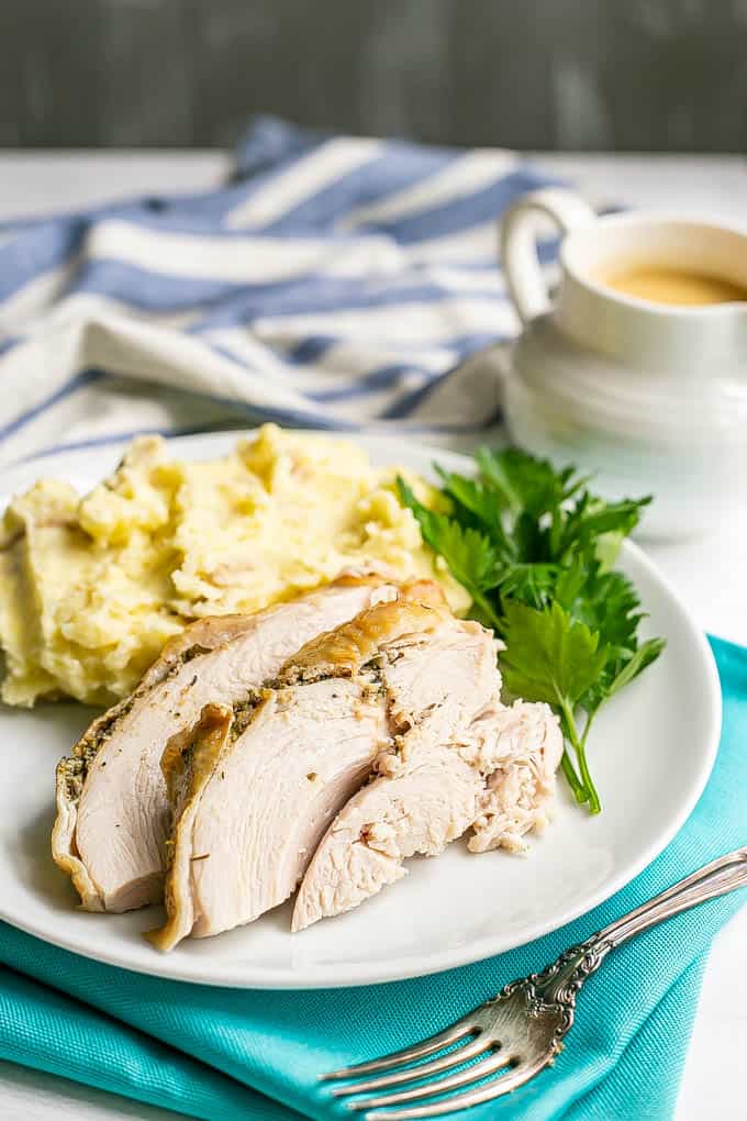 Sliced cooked turkey breast served on a white dinner plate with mashed potatoes and parsley