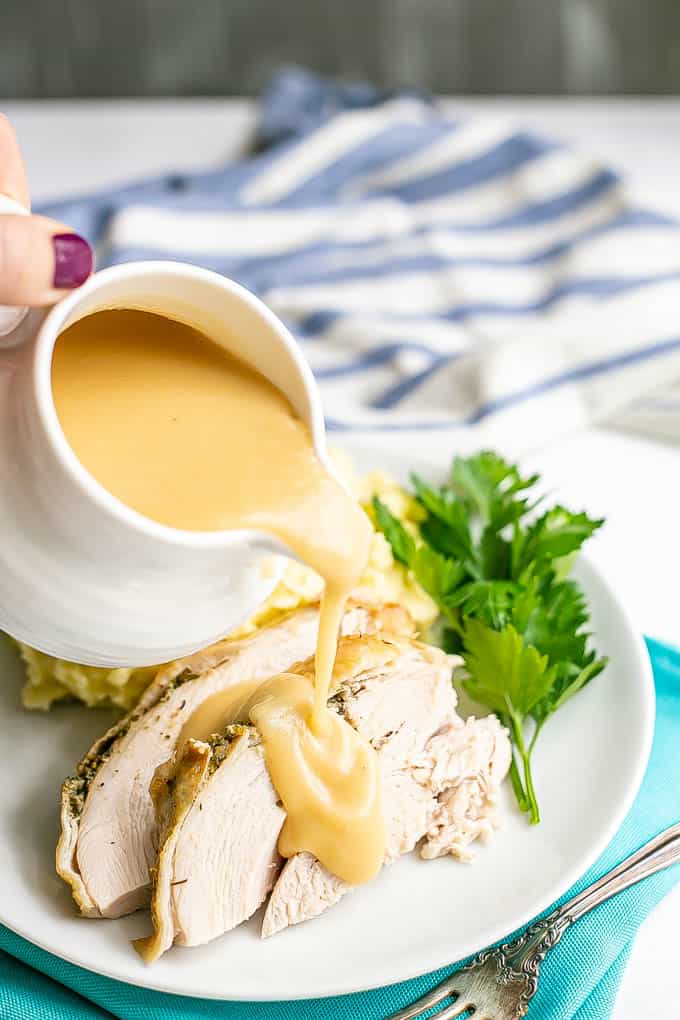 Gravy being poured from a white gravy dish over sliced turkey breast on a white dinner plate