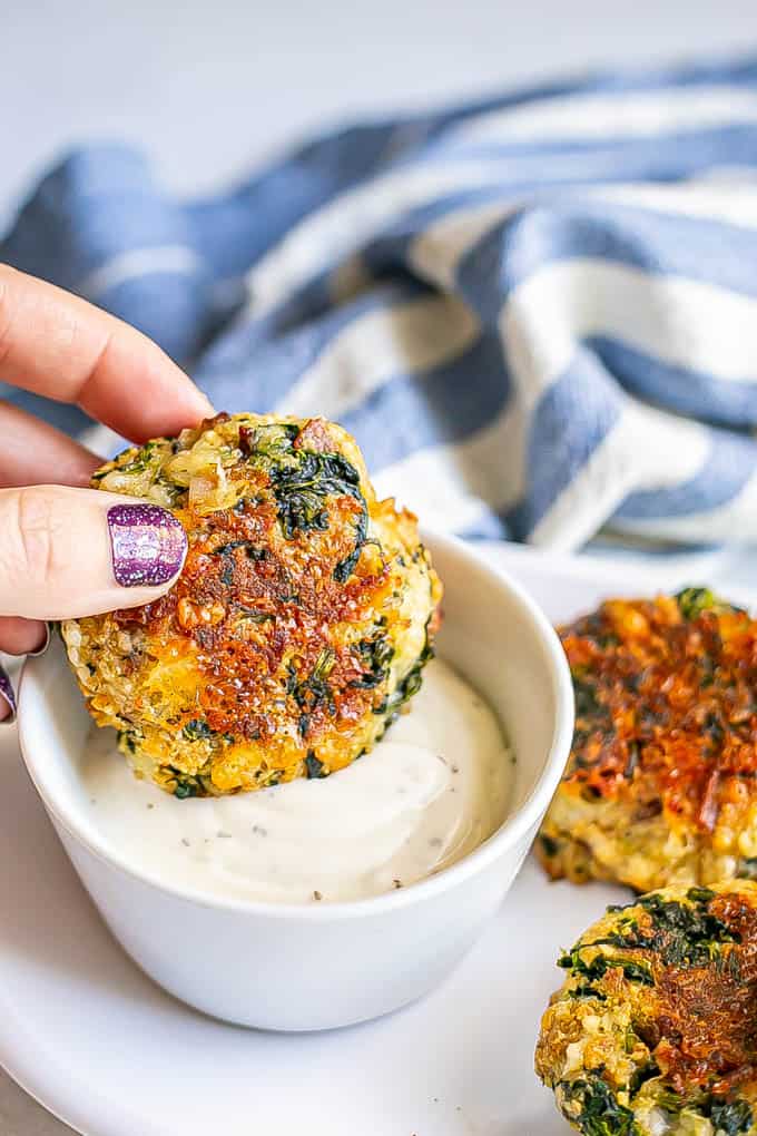 A hand dipping a baked cheesy spinach bacon cake into a bowl of Ranch dressing