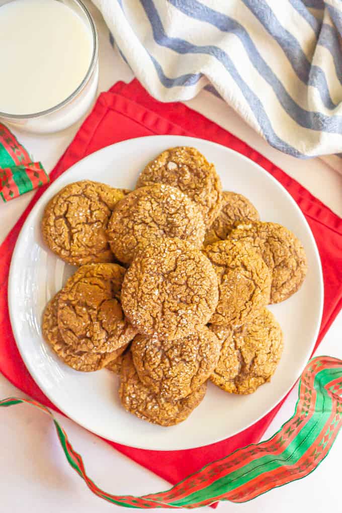 Overhead shot of a white plate stacked with ginger cookies and a glass of milk nearby