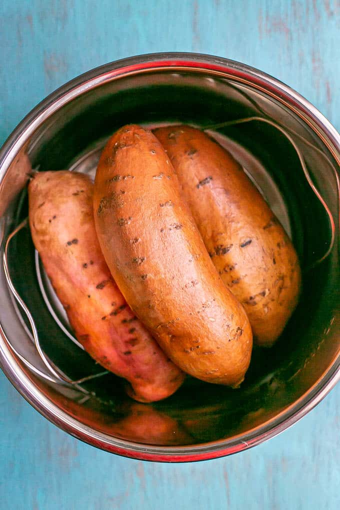 Three sweet potatoes placed on a trivet in the insert of an Instant Pot before being cooked