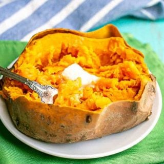 A fork resting in a cooked sweet potato with butter on top