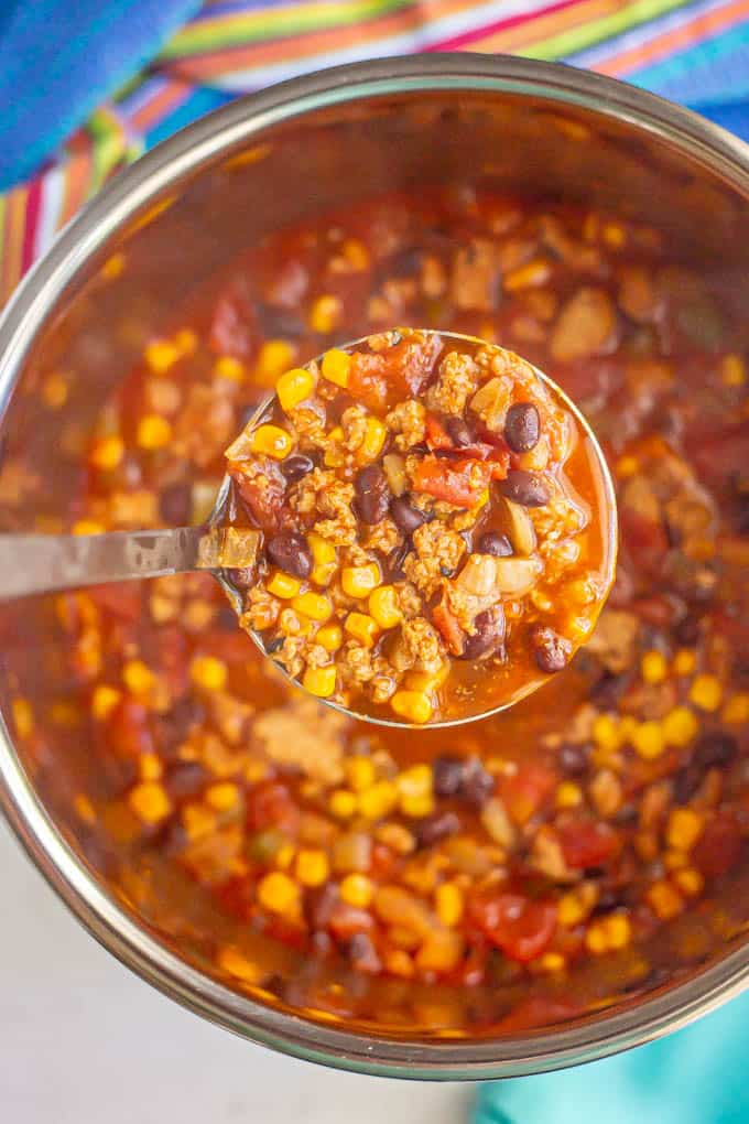 A ladle full of turkey chili with black beans and corn lifted from an Instant Pot insert