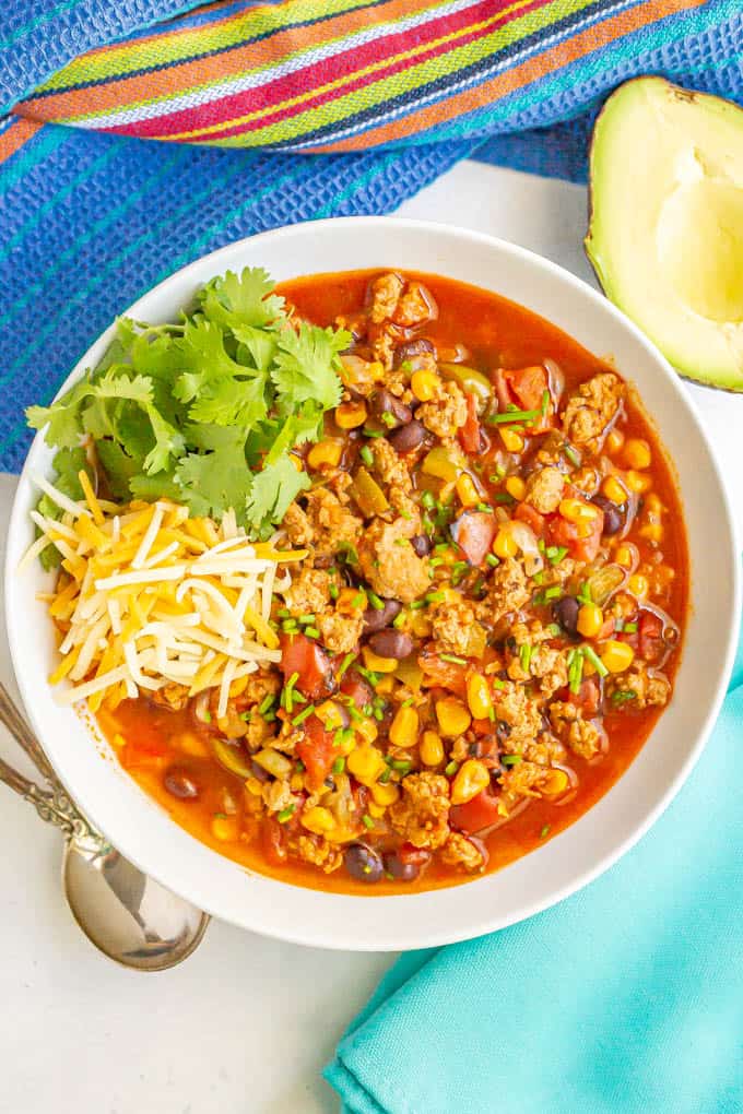 A white serving bowl filled with turkey chili and topped with shredded cheese and cilantro