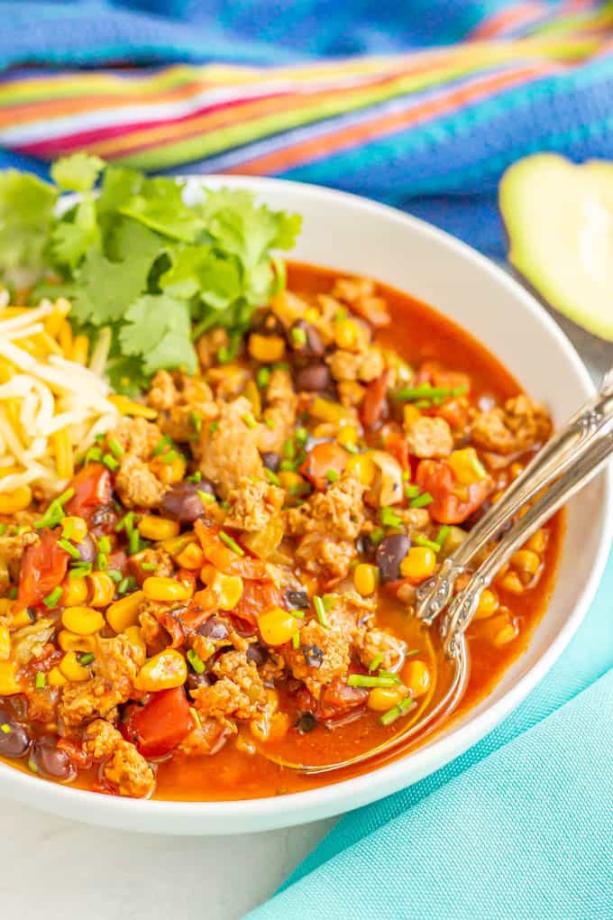 Two spoons resting in a bowl of ground turkey chili with black beans, tomatoes and corn