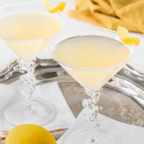 Two lemon drop martinis with lemon wedges for garnish set on white napkins in a silver serving tray