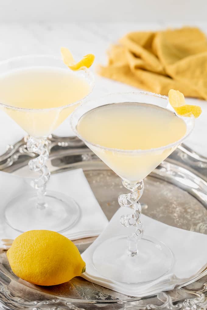 Two lemon drop martinis with lemon wedges for garnish set on white napkins in a silver serving tray