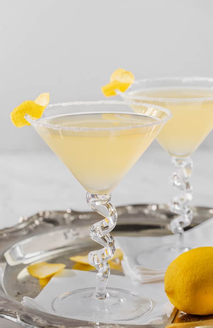 Two lemon drop martinis in glasses on a silver tray with lemon garnishes