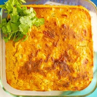 A glass dish of golden brown cheesy baked cornbread with a garnish of cilantro on the side