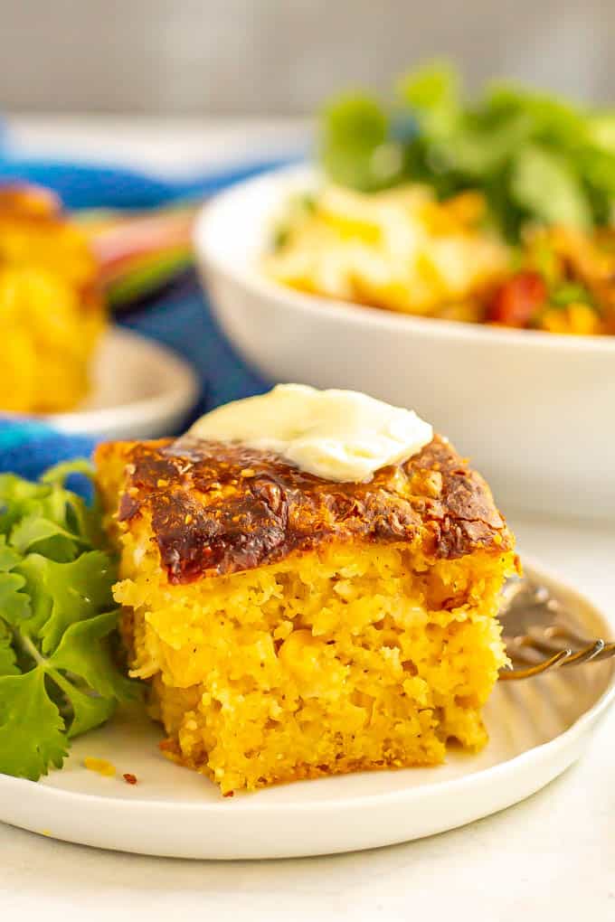 A piece of fluffy cornbread served on a small white plate with butter and a fork alongside