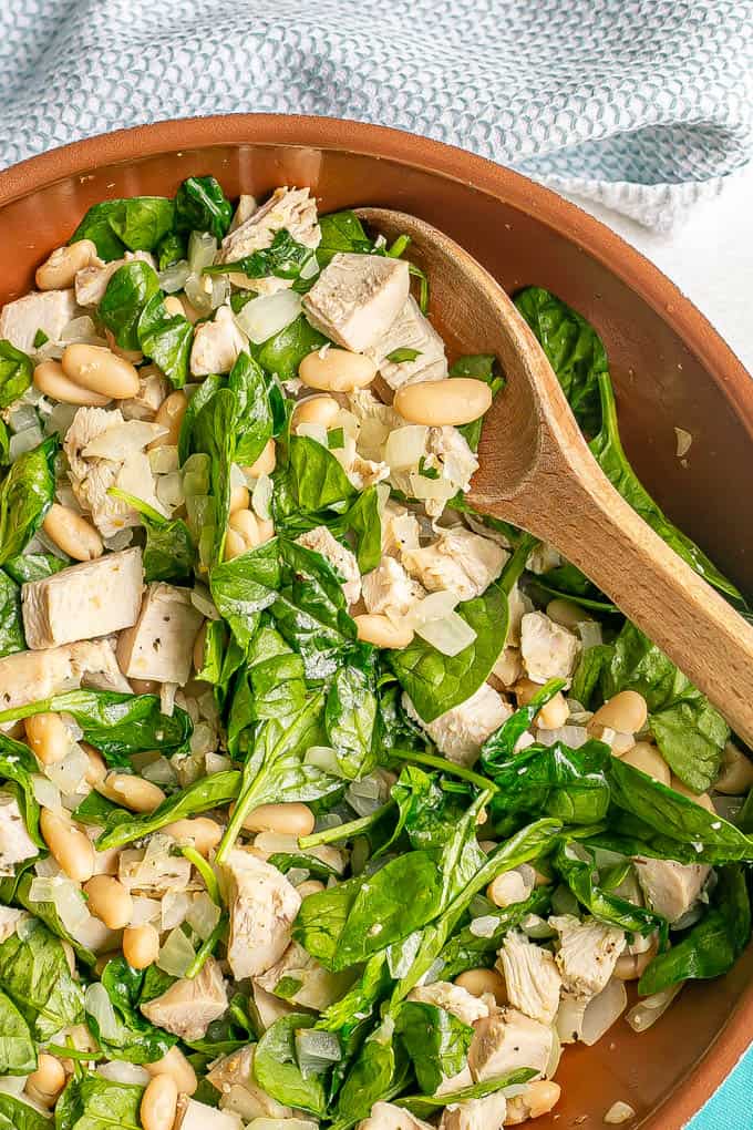 A wooden spoon scooping up some turkey, beans and spinach from a skillet
