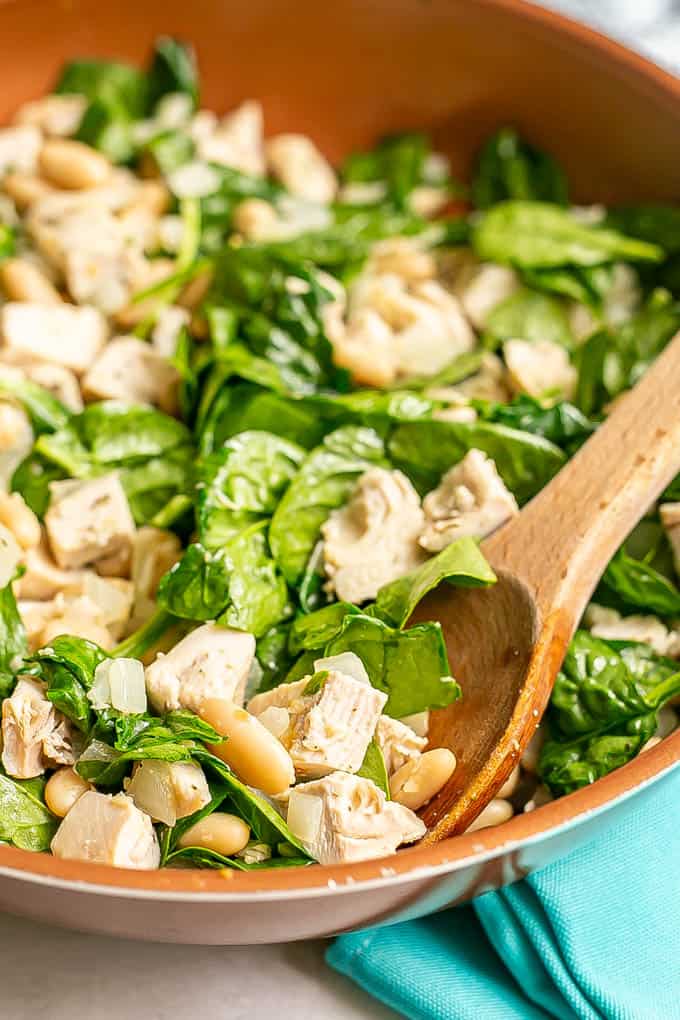 A wooden spoon scooping turkey, beans and spinach from a large copper skillet