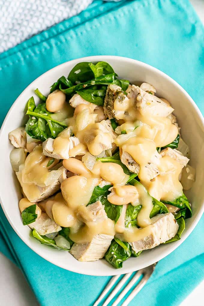 A bowl with spinach, beans and turkey with gravy on top and a fork nearby