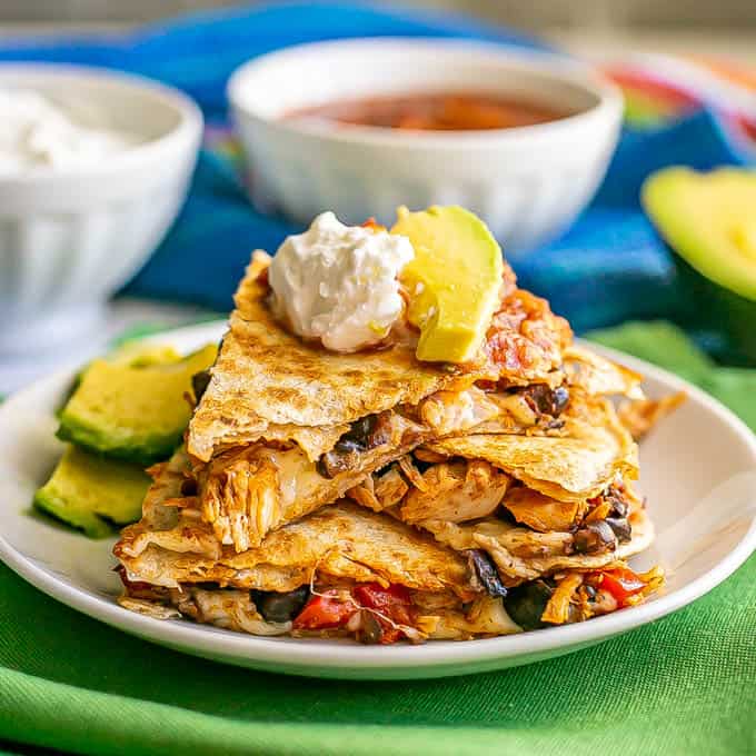 A sliced and served quesadillas with turkey, black beans and cheese, topped with salsa, Greek yogurt and avocado on a small white plate