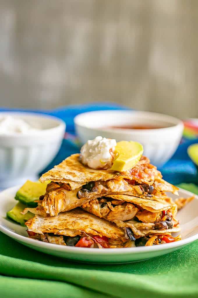 Turkey and black bean quesadillas stacked on a white plate with Greek yogurt, salsa and avocado on top