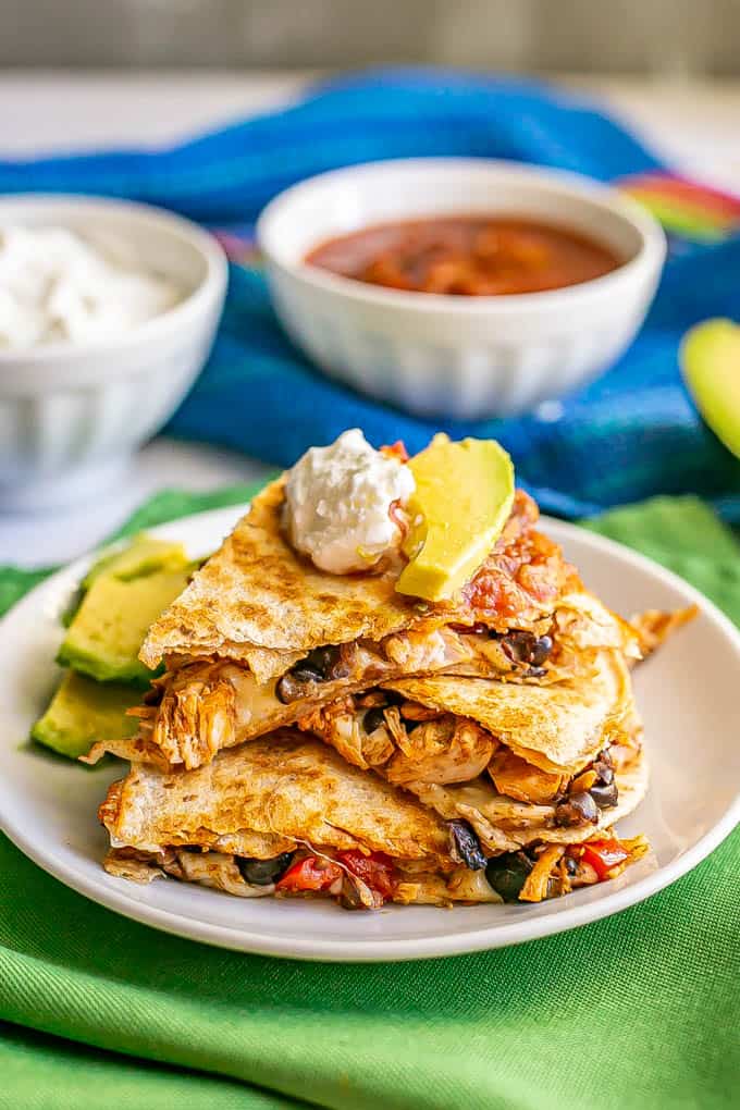 Turkey and black bean quesadillas stacked on a white plate with toppings on top and nearby
