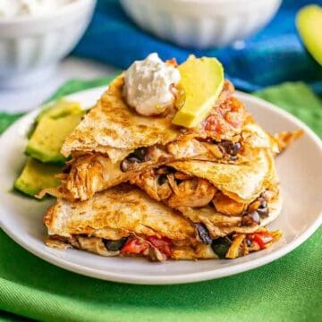 Turkey and black bean quesadillas stacked on a white plate with toppings on top and nearby