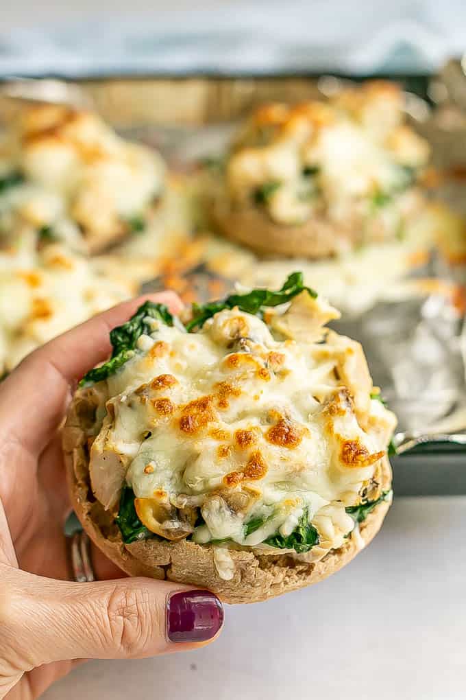 A hand holding an English muffin half with turkey, mushrooms and spinach and melted mozzarella on top
