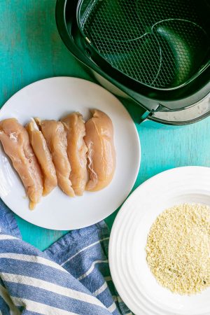 Chicken tenderloins on a plate near an Air Fryer with a separate bowl of a breadcrumb mixture for coating
