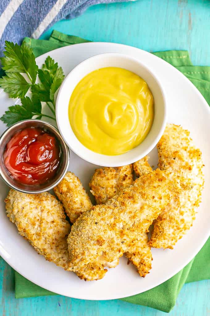 A plate of crispy chicken tenders with small bowls of ketchup and honey mustard for dipping