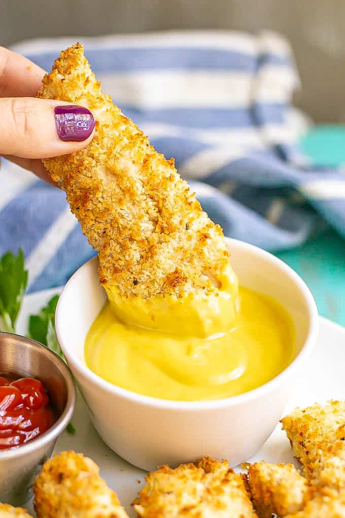 A crispy chicken tender being dipped in a small white bowl of honey mustard