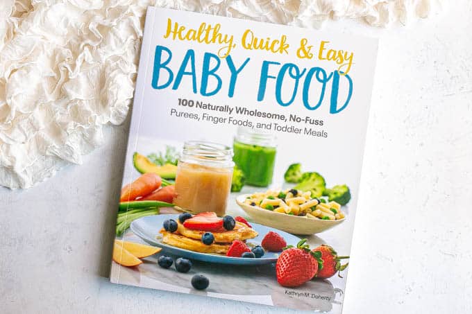 Cover of a baby food cookbook on a counter with a frilly white blanket