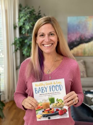 Author holding a copy of her baby food cookbook at home