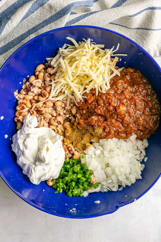 Black eyed peas, cheese, salsa and other ingredients layered in a large blue bowl before being mixed together