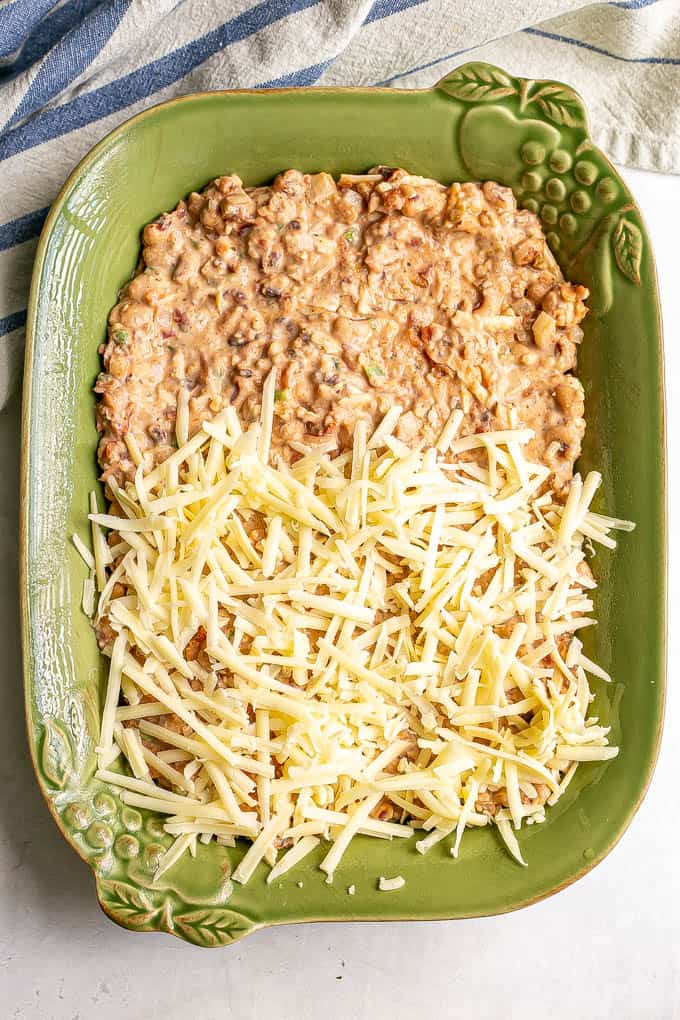 A creamy black eyed pea mixture in a casserole dish half covered with shredded cheese before baking