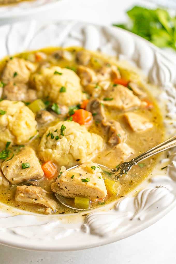 A spoon resting in a large white soup bowl of chicken and dumplings