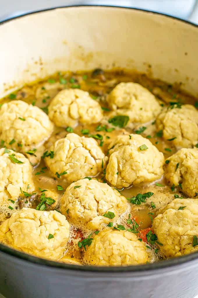 A side angle close up of dumplings floating on top of a chicken and vegetable stew in a large purple dutch oven
