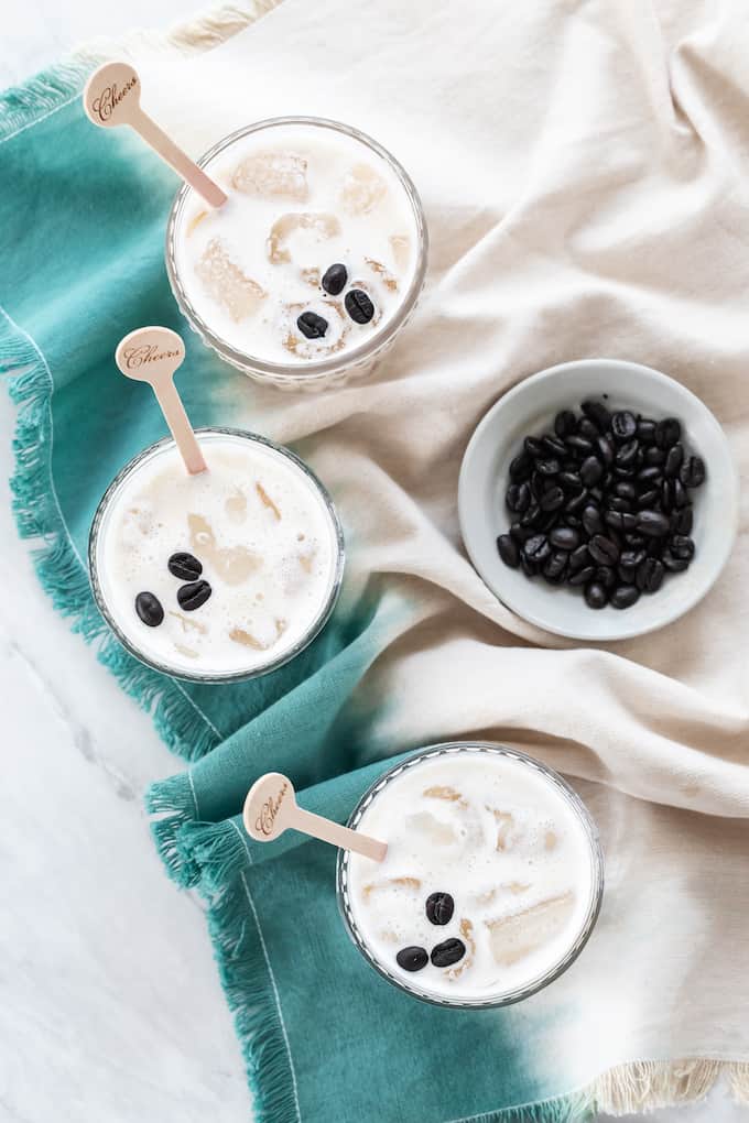 Three homemade white Russian drinks served in glasses with a bowl of coffee beans to the side.