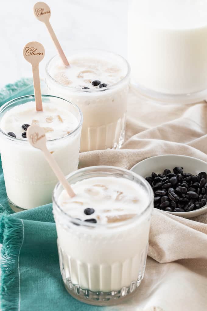 Three glasses filled with ice and an white Russian cocktail with coffee beans for garnish.