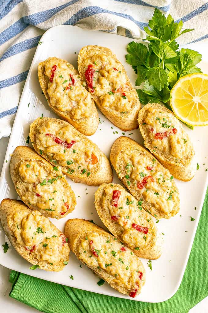 A white platter full of toasted crab melts sprinkled with chopped fresh parsley