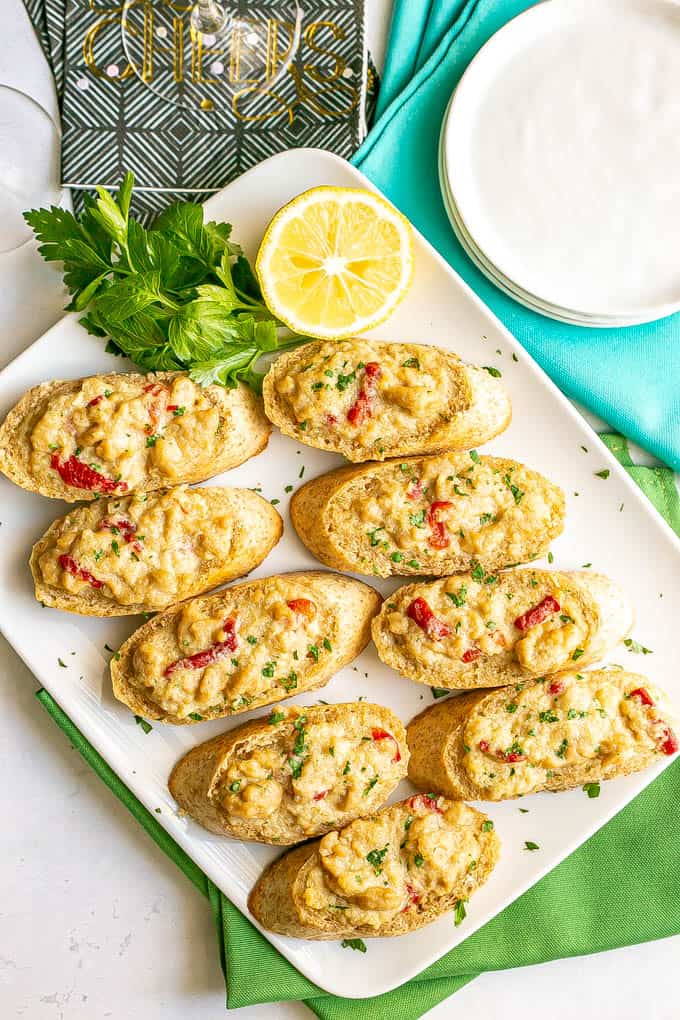 Baguette slices with a creamy crab mixture on top served on a white platter with lemon and parsley