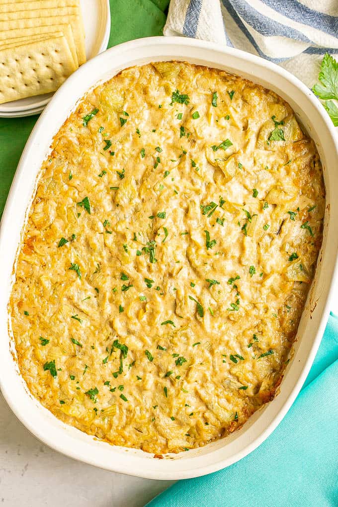 Baked artichoke dip with cheese in a casserole dish and topped with parsley