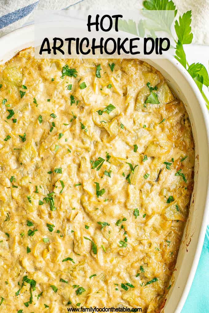 A creamy baked artichoke dip in a white casserole dish with a text overlay on top