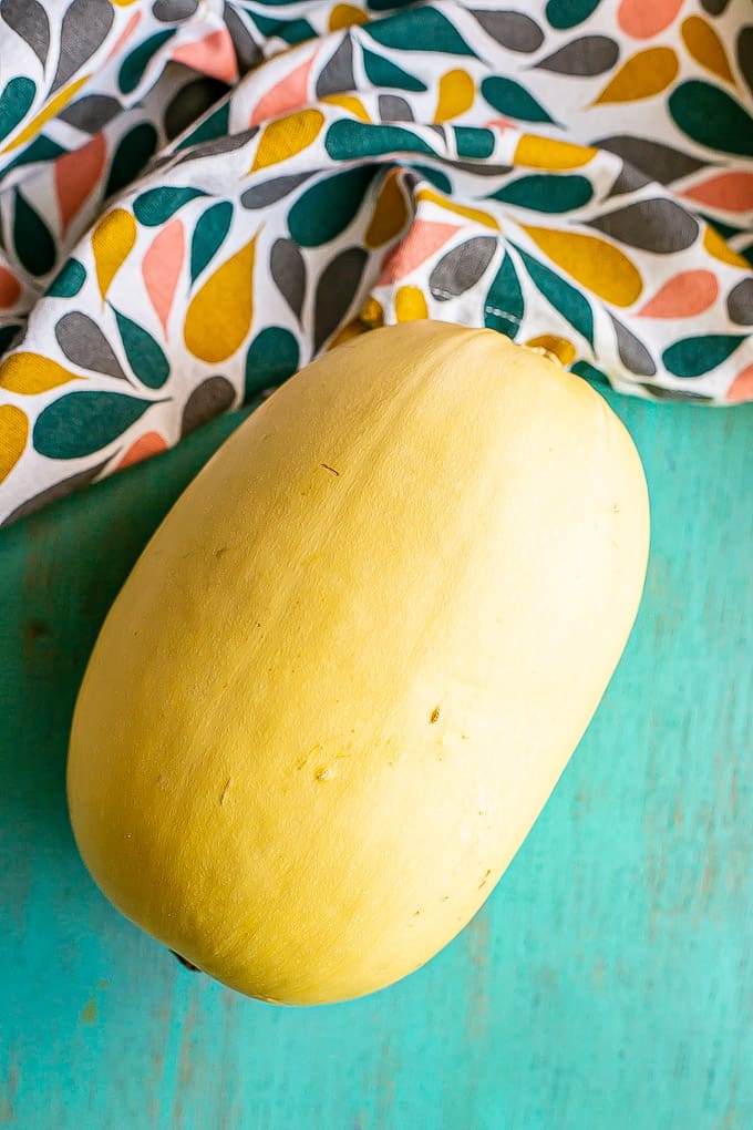 A whole spaghetti squash on a teal countertop with a colorful napkin nearby