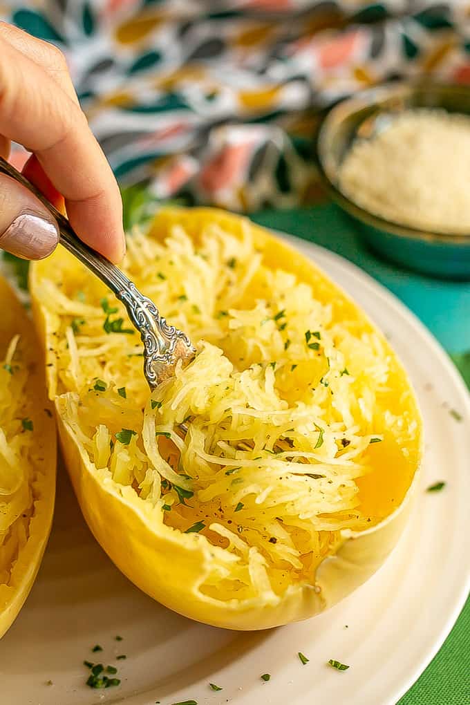 A fork twirling up some spaghetti squash strands from a halved spaghetti squash boat