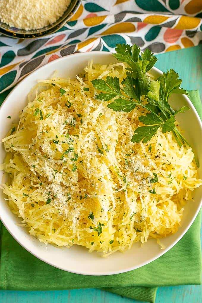 A white bowl full of cooked, pulled spaghetti squash strands sprinkled with Parmesan cheese and parsley