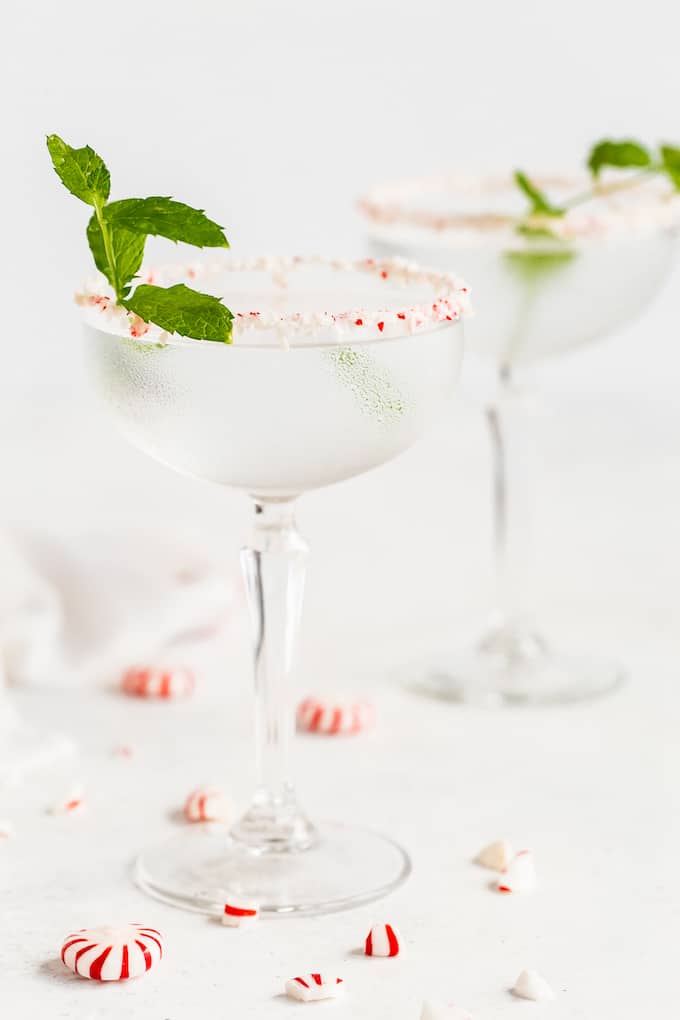 Two peppermint martinis in elegant glasses with sprigs of mint and crushed peppermints scattered