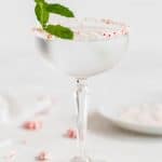 A peppermint rimmed martini glass with a peppermint martini and a sprig of mint with a text overlay on top