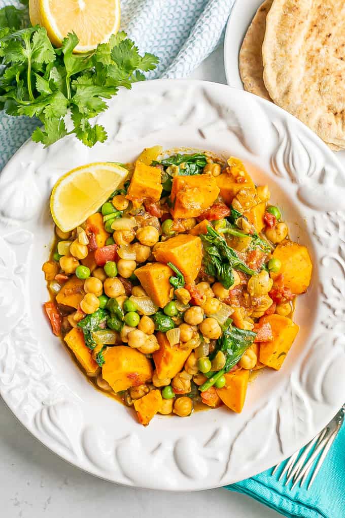 A white bowl full of a chickpea curry with sweet potatoes and spinach