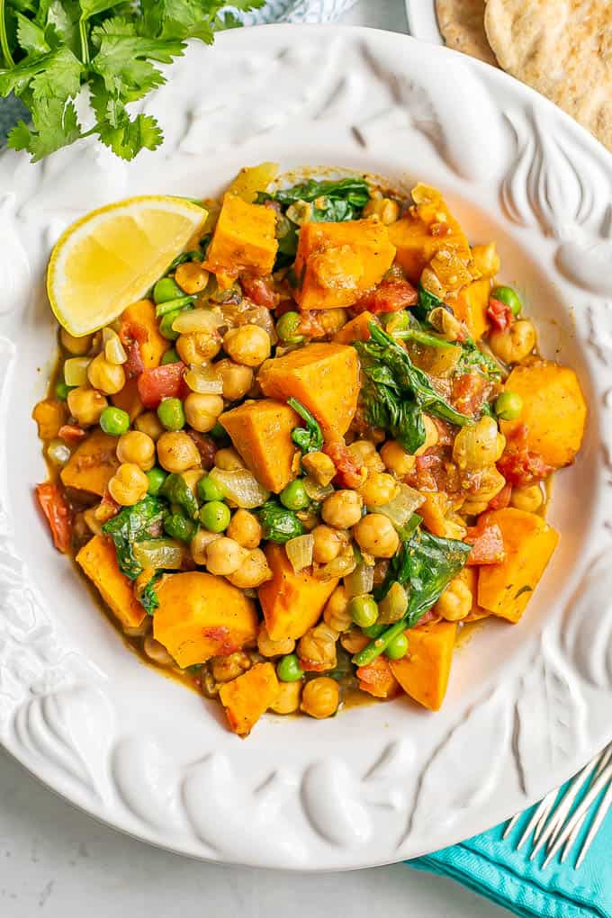 A bowl full of a chickpea and sweet potato curry with spinach and peas