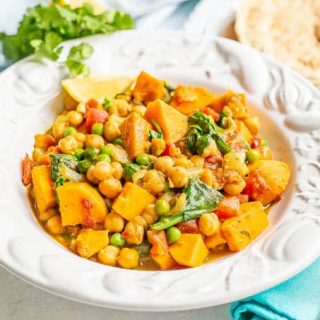 A white bowl filled with a chickpea curry with sweet potatoes and spinach