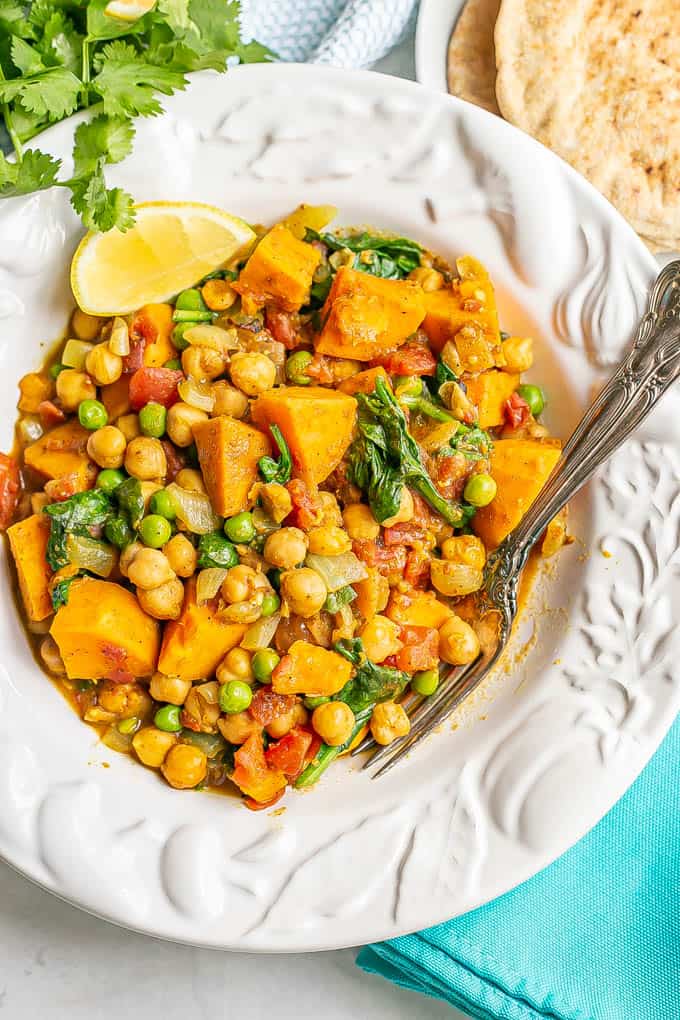 A soup bowl full of a vegetable curry with chickpeas and sweet potatoes with two forks resting in the bowl