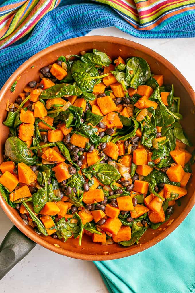 A vegetarian skillet meal with sweet potatoes and black beans and wilted spinach